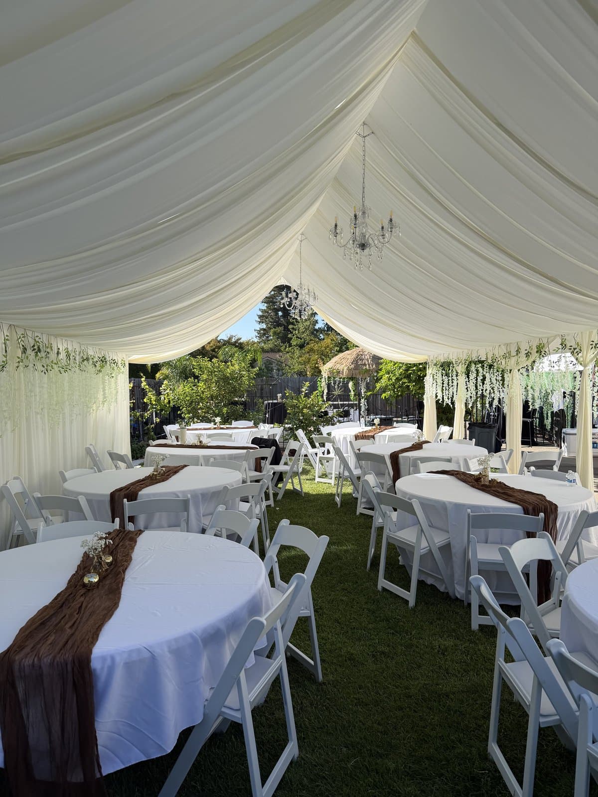 White frame tent in a backyard with round tables, white chairs and draped ceiling