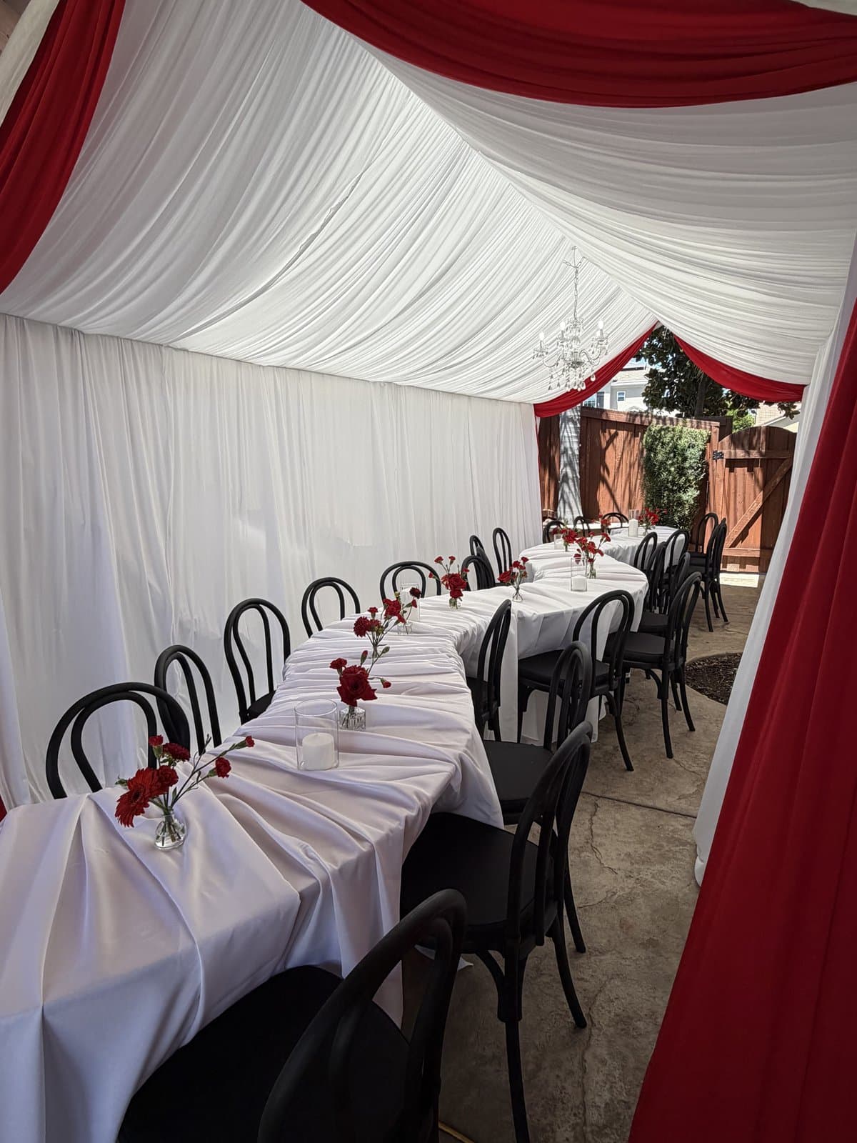 Long banquet tables with white linens, black chairs and red floral centerpieces inside a tent
