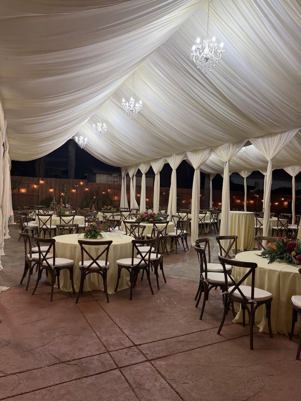 Draped tent lit by crystal chandeliers over round tables and cross-back chairs at a Sacramento evening event