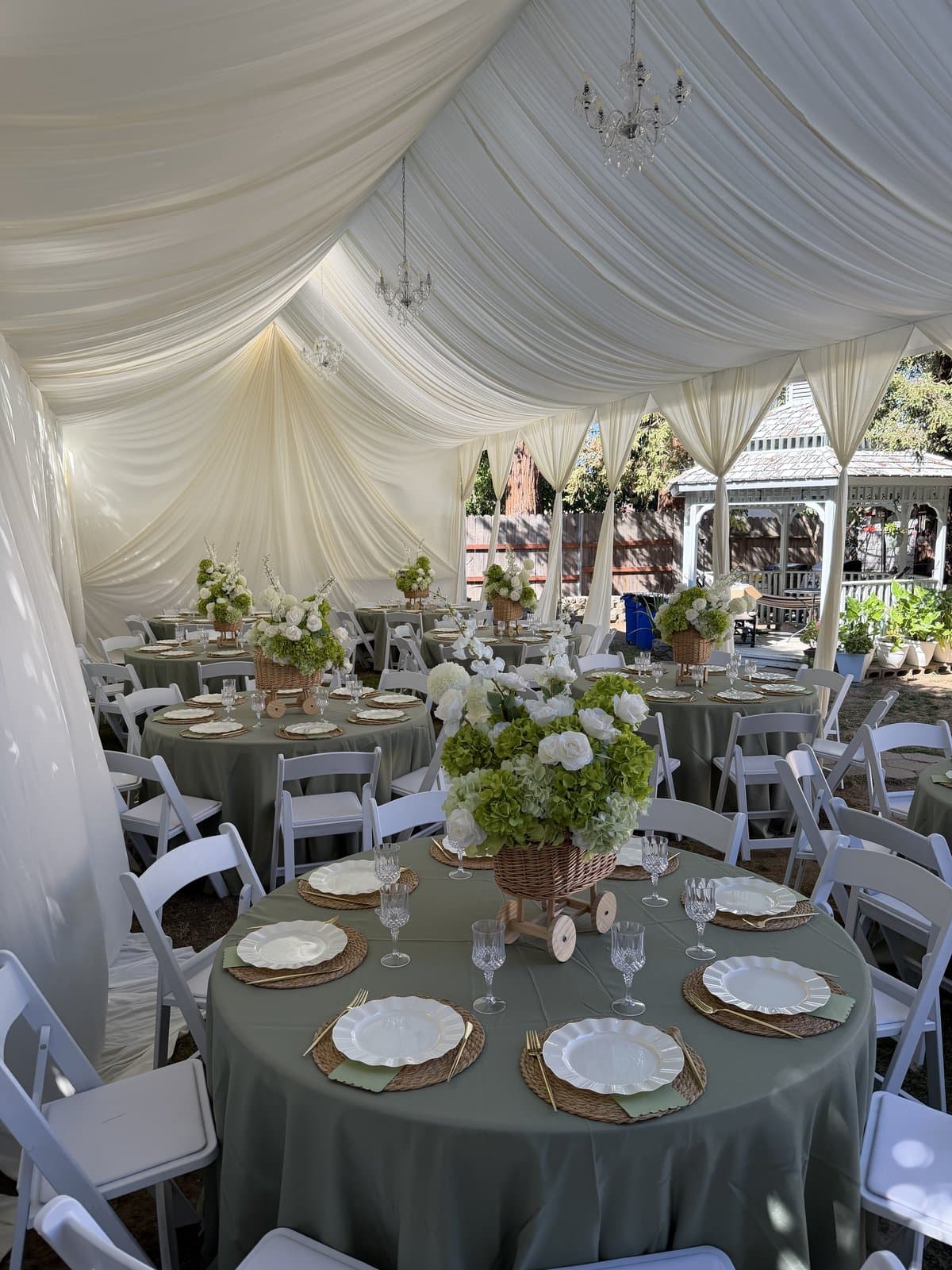 Round tables with sage linens, floral centerpieces and white chairs under a draped tent