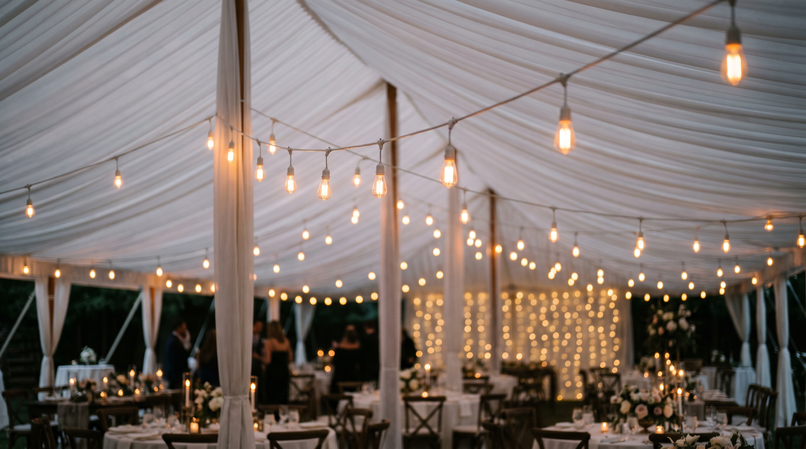 String lights and chandeliers illuminating an outdoor event tent at night